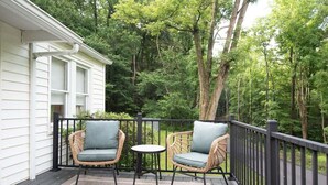 A covered outdoor area with wicker chairs and a small table, surrounded by a wooden deck and a black railing.