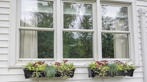 A window with three panes, each with a black hanging planter containing various plants.