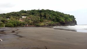 A beach with a rocky cliff and a building with multiple stories. - El Patio de Don Moncho - Shalpa (Jicalapa)