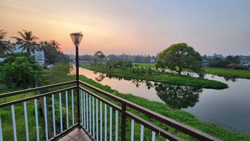 Enjoy a serene riverside view from your balcony, overlooking a calm water body surrounded by lush greenery and distant buildings.