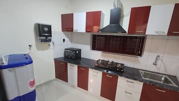 A compact kitchen with red and white cabinets, a built-in microwave, a gas stove, and a wall-mounted oven.