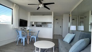 A modern living room with a grey sofa, a round coffee table, and a ceiling fan. - Heart of Waikiki w/ Kitchen - Free Parking - Ocean View - King Bed - Corner Unit (Honolulu)