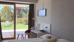 Una habitación de hotel moderna con una cama grande, un escritorio, una silla, un televisor y un gran ventanal corredizo que da a un patio.