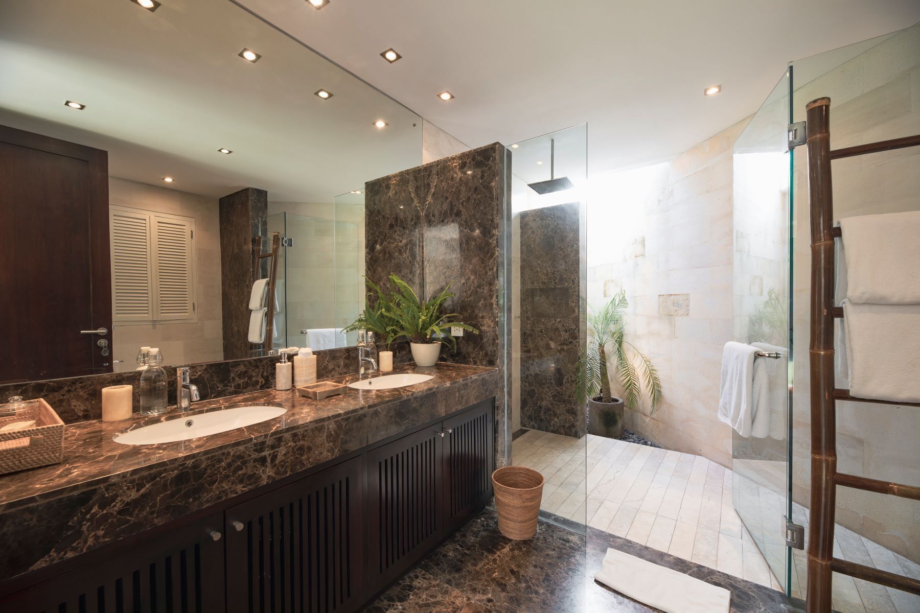 A modern bathroom with a marble vanity, a glass shower enclosure, and a potted plant.