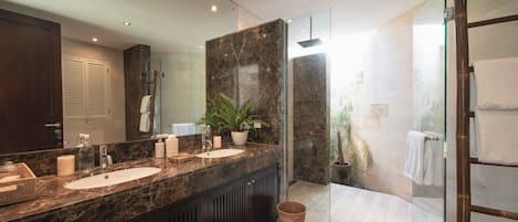 A modern bathroom with a marble vanity, a glass shower enclosure, and a potted plant.