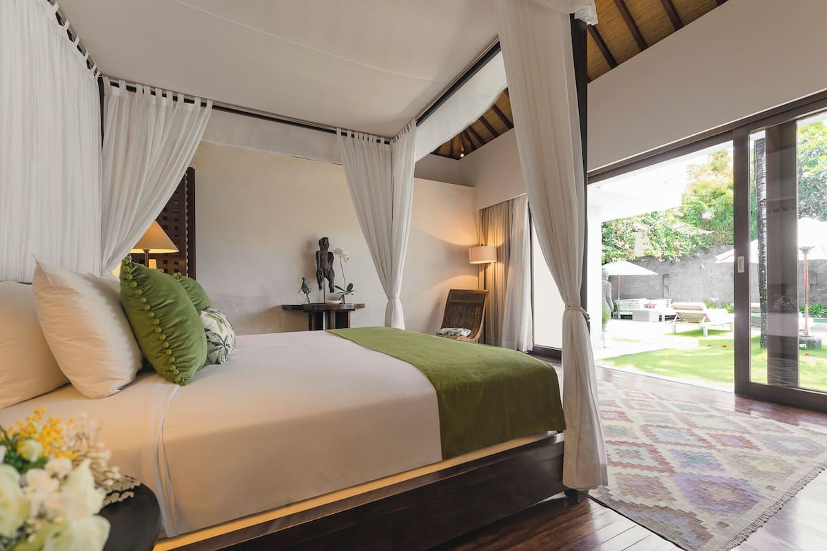 A spacious bedroom with a large bed, a nightstand, a chair, and a view of the garden through a glass door.