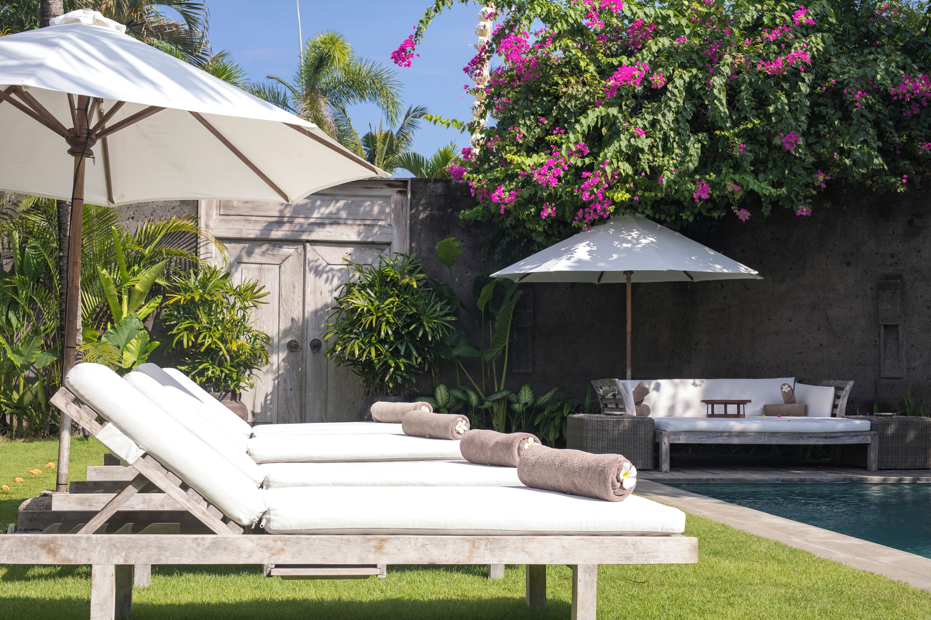 A poolside area with lounge chairs, a sofa, and umbrellas.