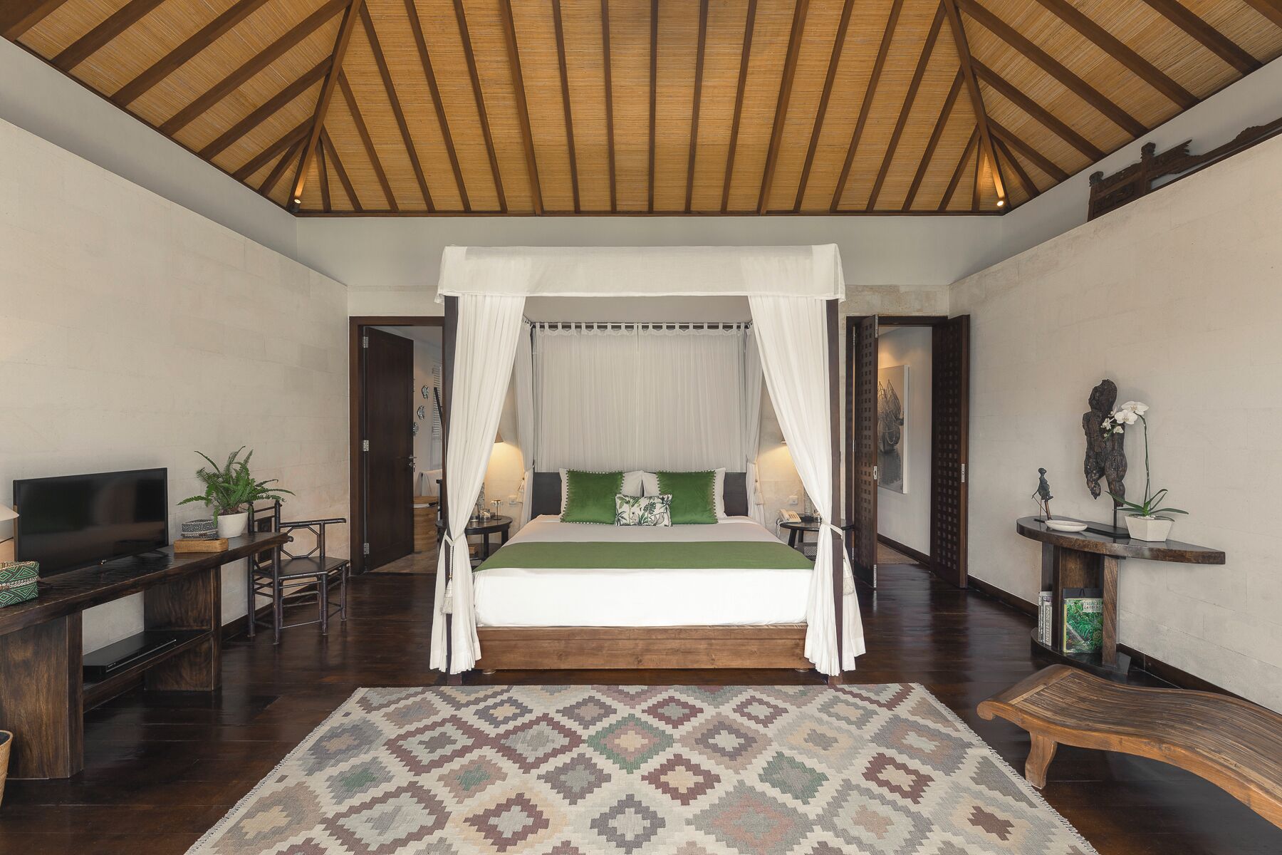 A bedroom with a canopy bed, wooden flooring, a television, and a desk with a chair.