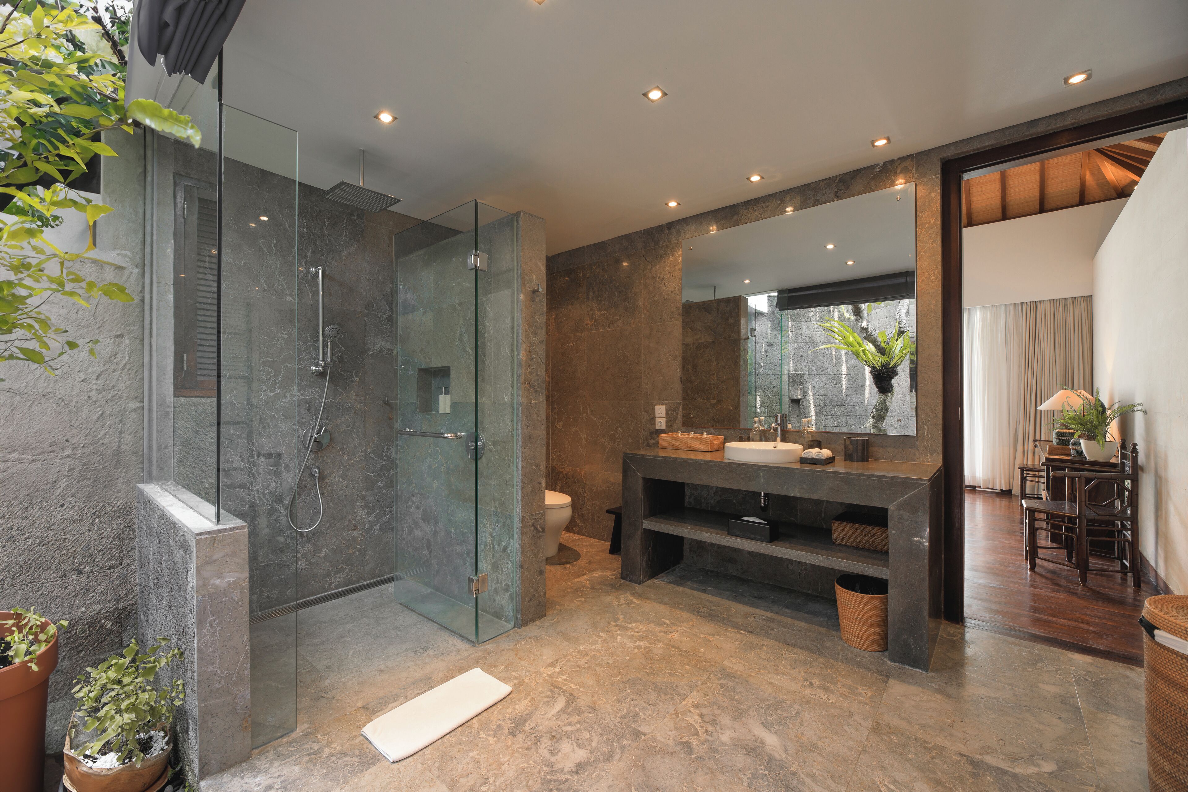 A modern bathroom with a glass-enclosed shower, marble flooring, and a large mirror.