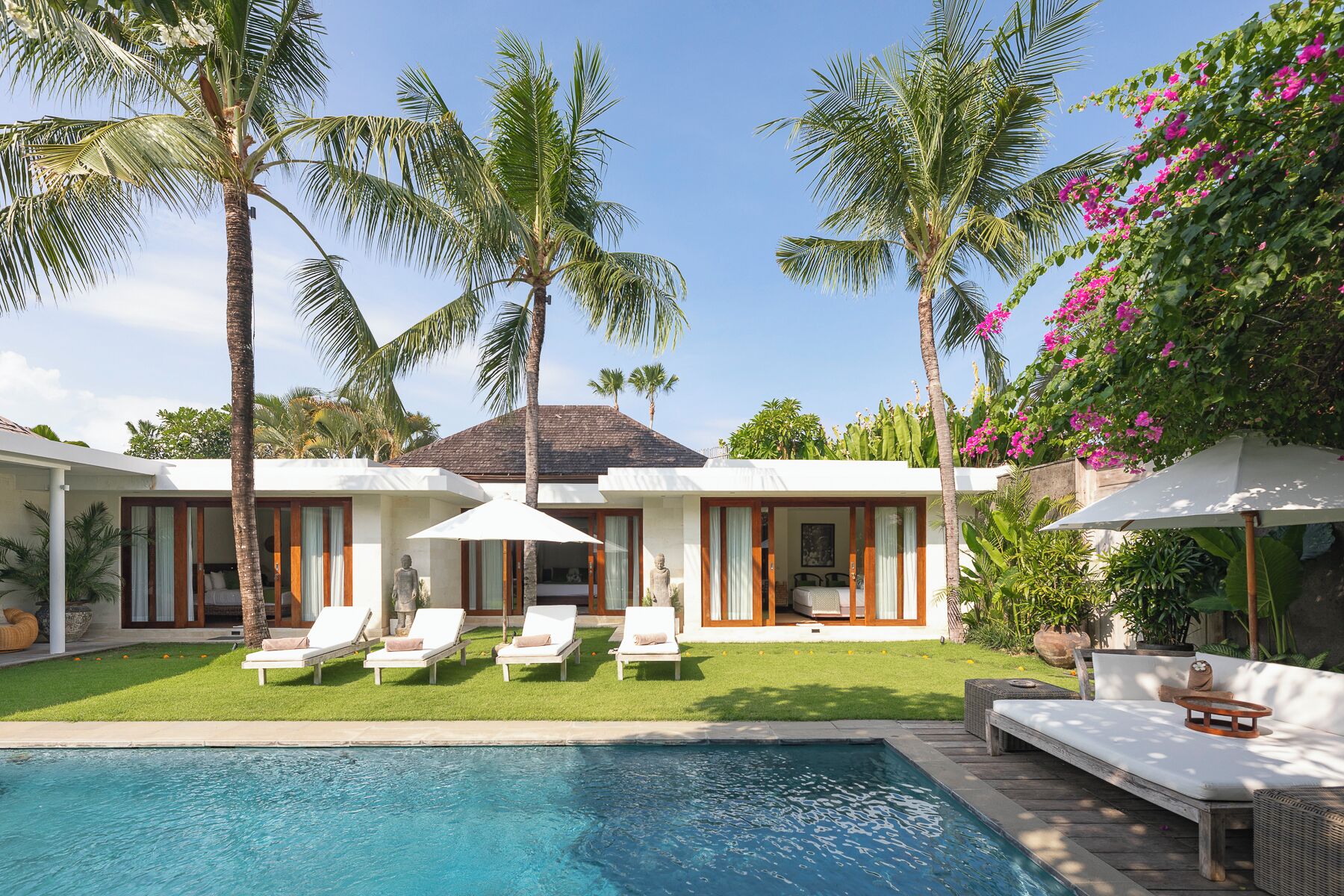 A modern villa with a pool, lounge chairs, and tropical plants.