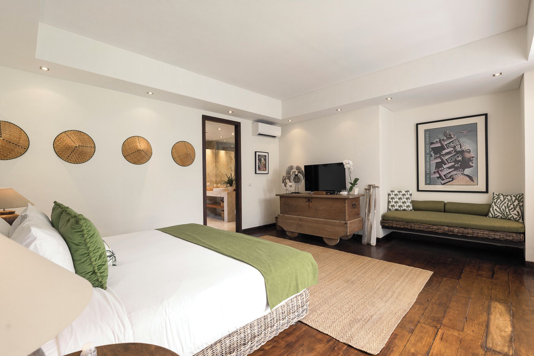 A bedroom with a bed, a TV, a sofa, and a bathroom visible through an open door.