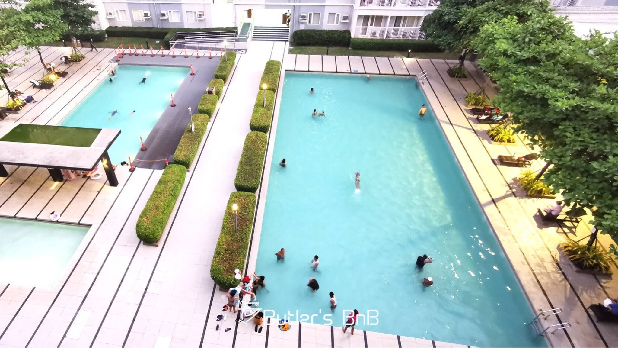 A rooftop swimming pool with multiple lanes and a separate shallow area, surrounded by lounge chairs and potted plants.