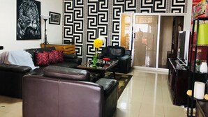 A living room with a black and white patterned wall, a black leather sofa, a coffee table with a vase of flowers, and a television on a wooden stand. - Serene one bedroom apartment in a quiet residential area, privacy assured  (Accra)