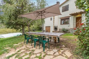 Eine Terrasse mit Tisch und Stühlen, einem großen Sonnenschirm und einem Haus im Hintergrund.