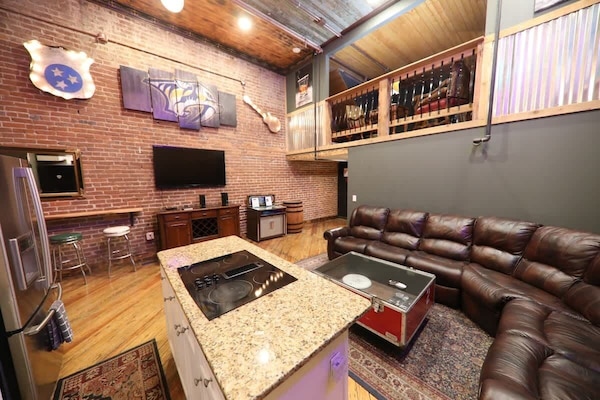 The balcony of the speakeasy overlooks the large seating and kitchen area with a coffee table made from an old road case. A large flat-screen tv is available for entertainment.