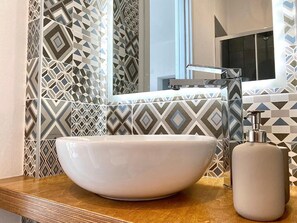 Une salle de bain avec un grand lavabo blanc posé sur un plan de travail en bois, un miroir et des carreaux décoratifs sur le mur.