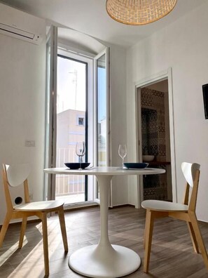 Un coin repas avec une table ronde blanche, deux chaises en bois et un luminaire suspendu.