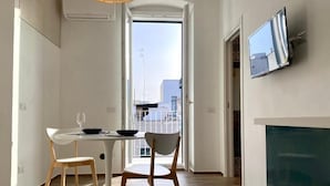 Un espace repas moderne avec une table ronde, deux chaises et une vue sur l’extérieur, accessible par une porte ouverte.