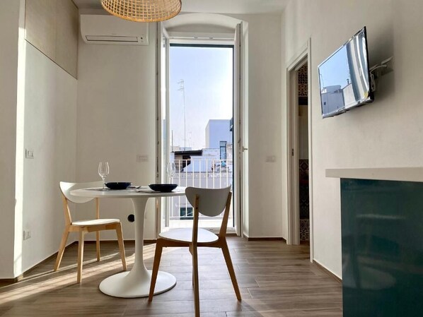 Un espace repas moderne avec une table ronde, deux chaises et une vue sur l’extérieur, accessible par une porte ouverte.