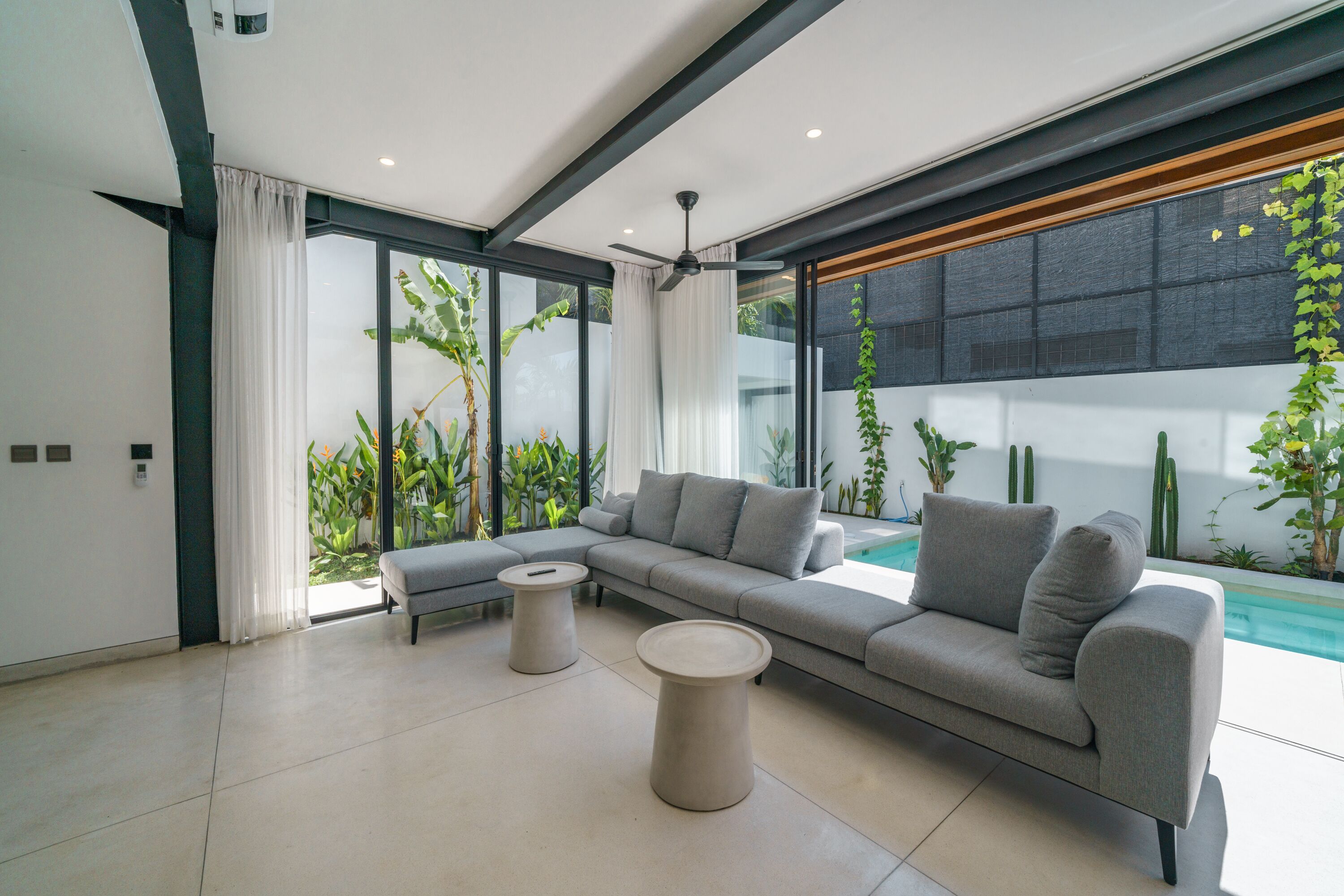 A modern living room with a sectional sofa, two round coffee tables, and a large window overlooking a pool.