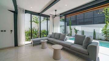 A modern living room with a sectional sofa, two round coffee tables, and a large window overlooking a pool.