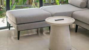 A modern living room with a grey sectional sofa, a round coffee table, and a large window with a view of indoor plants. - Villa Vantage 7 (Kerobokan)