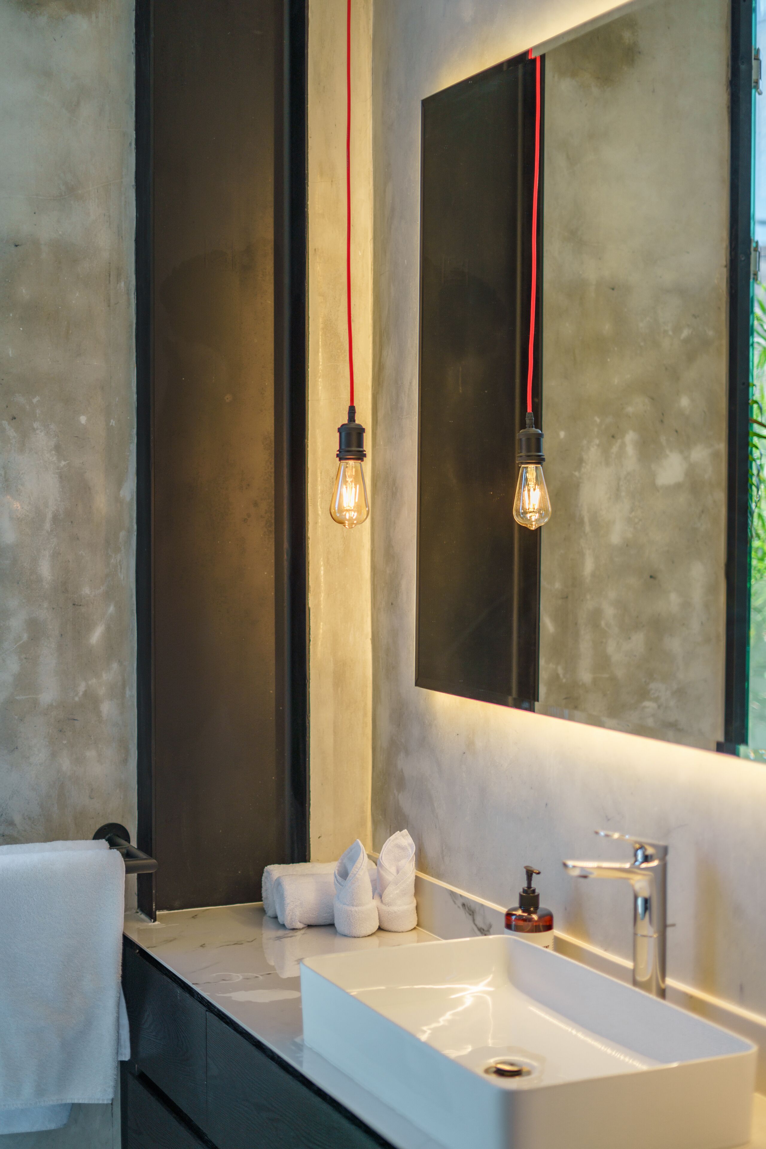 A modern bathroom with a large mirror, a white sink, and two exposed light bulbs.