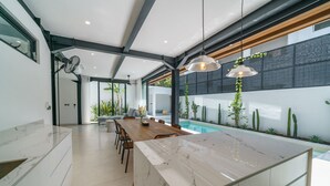 A modern kitchen with a marble island, wooden dining table, and a built-in pool. - Villa Vantage 7 (Kerobokan)