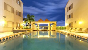 A swimming pool with lounge chairs, a covered area, and a view of a building at dusk. - Hope Harbour Hotel Apartments (Hope Island)