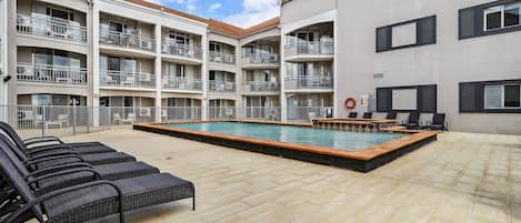 A multi-story building with balconies, a swimming pool, and outdoor seating.