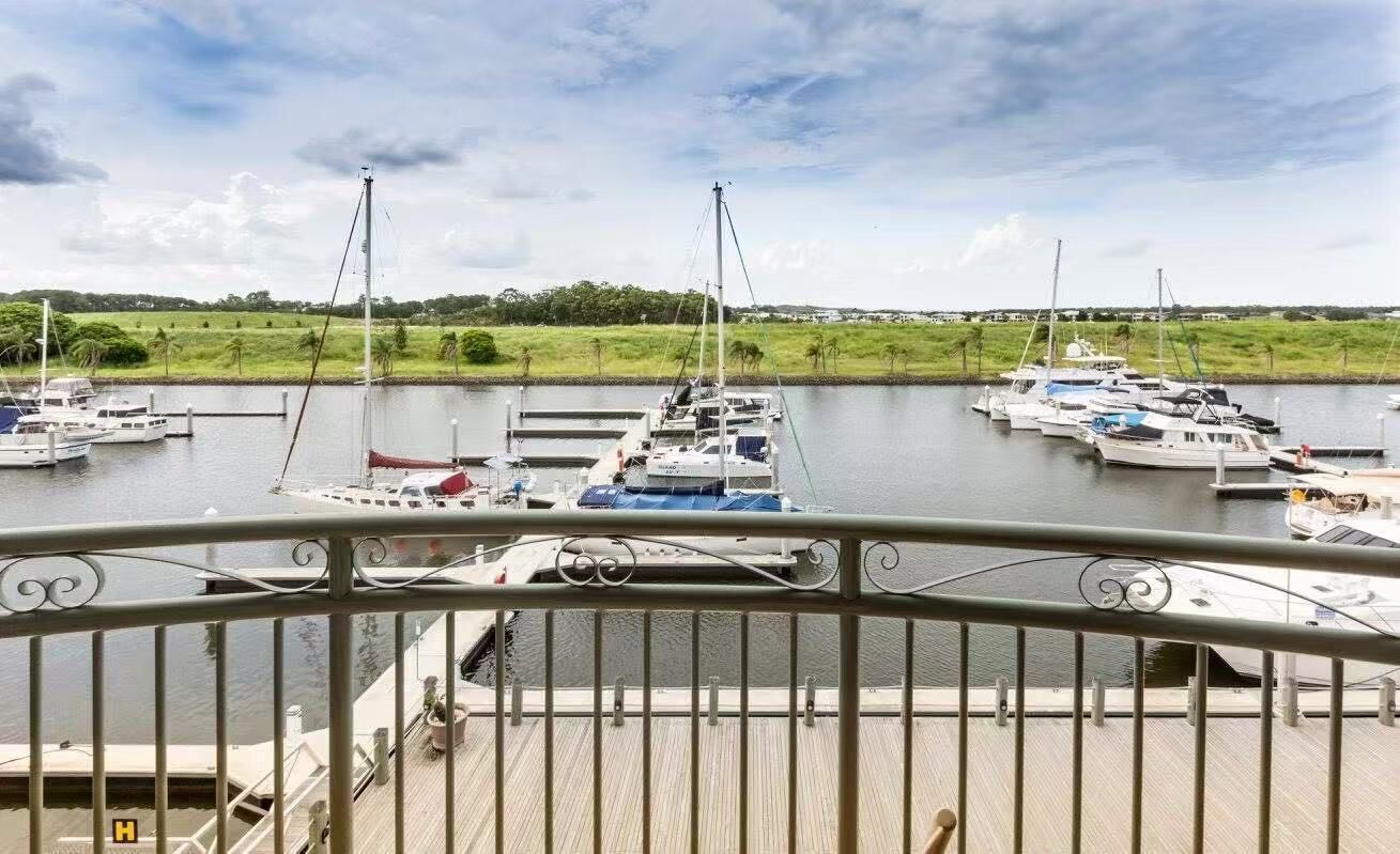 A marina with multiple boats docked, a grassy landscape in the background, and a wooden deck with railings in the foreground.