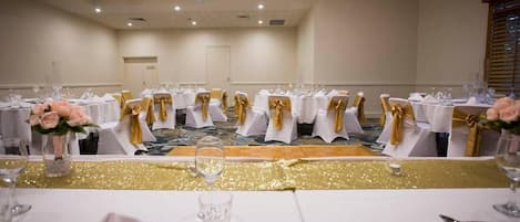 A banquet hall with round tables, each with white tablecloths and gold sashes, set for a formal event.