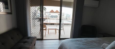Habitación de hotel con cama, sofá y puerta corrediza de vidrio que da a un área exterior con mesa y sillas.