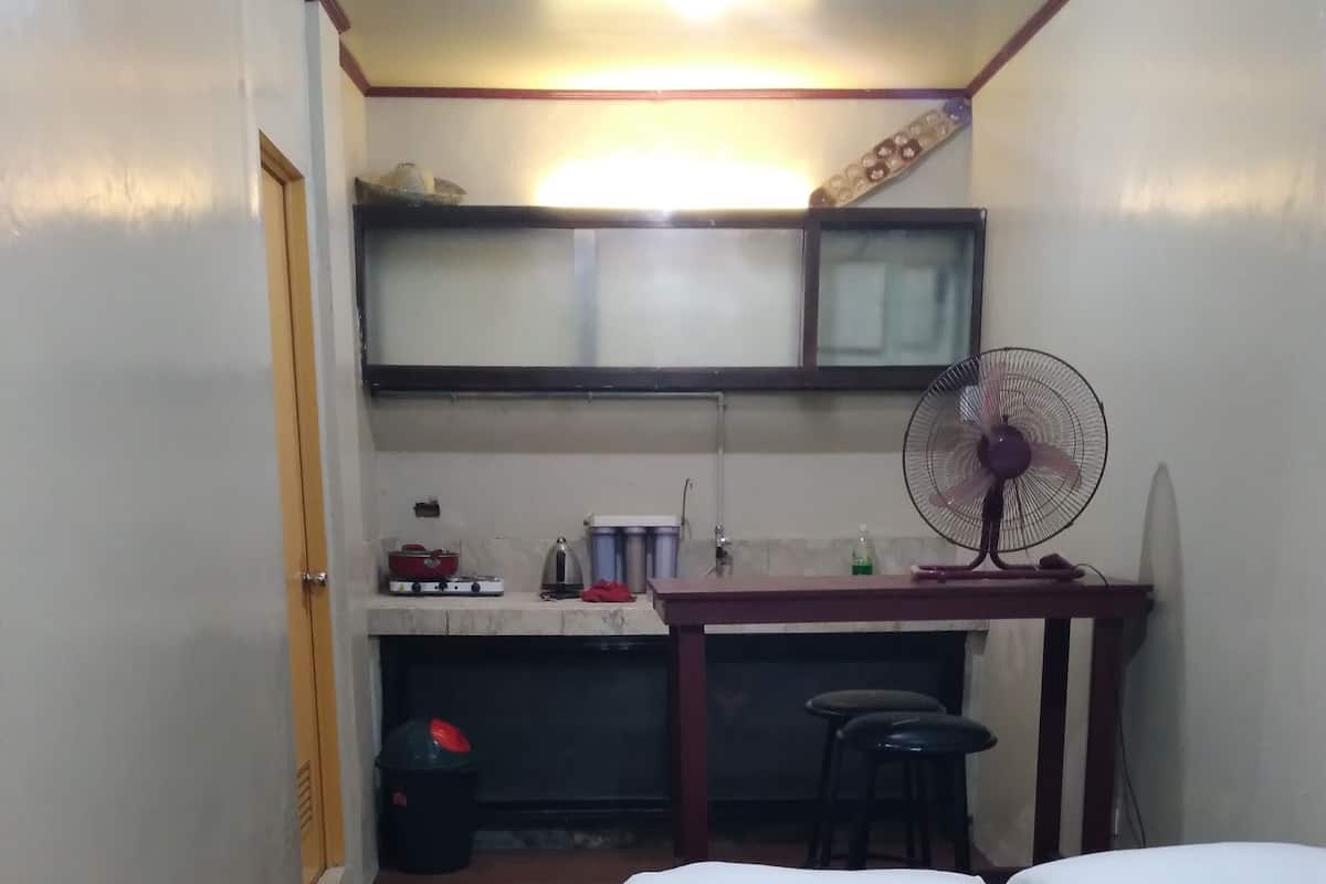 A small, compact room with a bed, a desk, a chair, a fan, and a mirror.