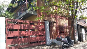 A gated residential area with a red gate, a motorcycle parked nearby, and a tree casting shadows on the ground. - TerisitaPlace Otél (Taytay)