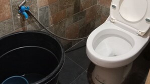 A bathroom with a toilet, a black bucket, and a blue hose. - TerisitaPlace Otél (Taytay)