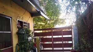 A narrow alleyway with a yellow building on one side and a red gate on the other. There are potted plants and a motorcycle parked along the alley. - TerisitaPlace Otél (Taytay)