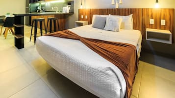 Een moderne slaapkamer met een groot bed, een houten hoofdbord, nachtkastjes en een keuken in de achtergrond.