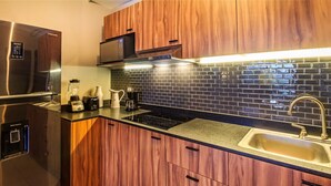 Una cucina moderna con mobili in legno, un frigorifero in acciaio inossidabile, un forno a microonde integrato e uno schienale rivestito in piastrelle nere.