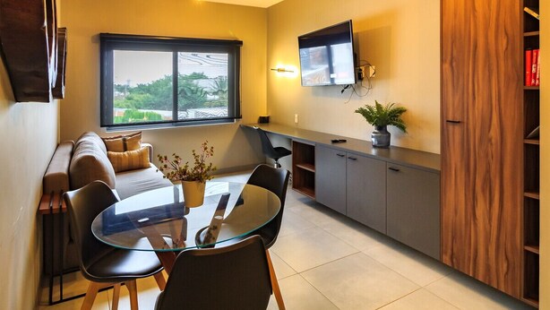 Un soggiorno moderno con un tavolo da pranzo in vetro, sedie nere, un divano, una TV a parete e un mobile contenitore in legno.