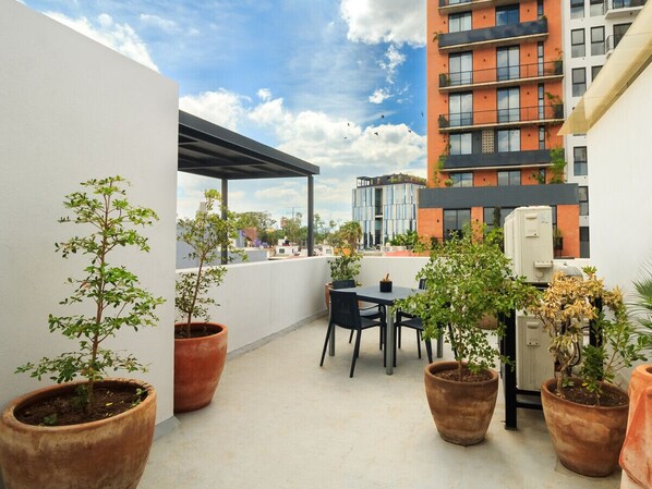 Enjoy panoramic views from this rooftop seating area, surrounded by lush greenery and a cityscape.