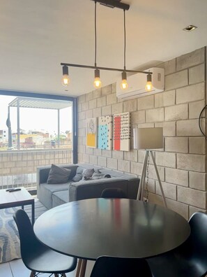 Un salon moderne avec un canapé gris, une table ronde et un luminaire suspendu au plafond.