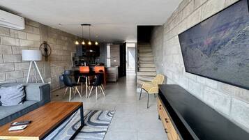 A modern living space with a sofa, coffee table, dining area, and a large TV mounted on the wall.