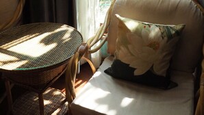 A wicker chair with a cushion, a small round table, and a window with curtains.