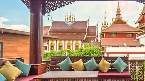 An outdoor seating area with wooden furniture and a view of traditional Thai architecture.