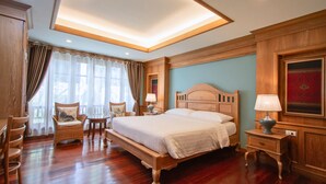 A spacious bedroom with a large bed, wooden headboard, and a nightstand with a lamp. There is a chair and a small table with a lamp in the corner.