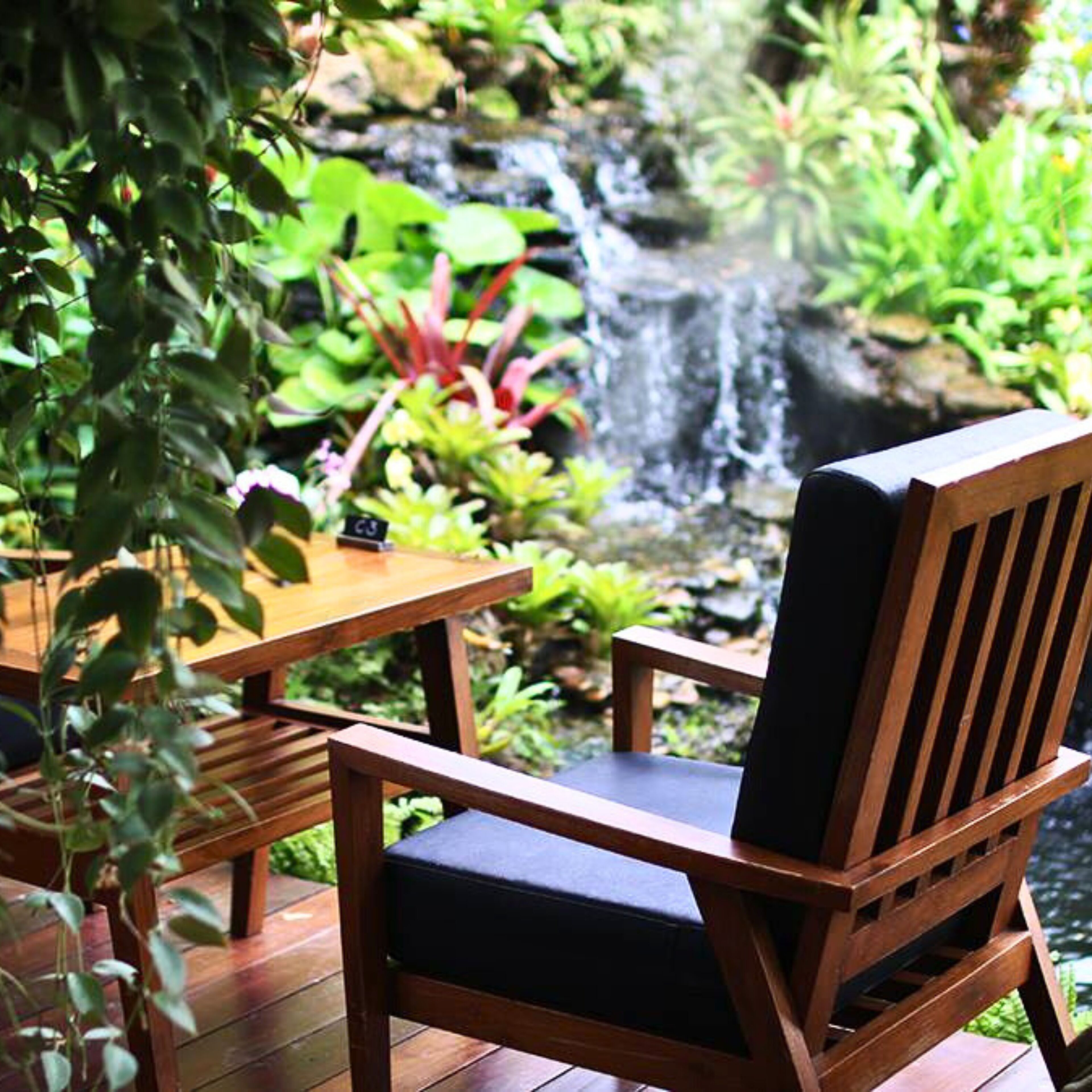 Una silla de madera con cojín, una mesa de madera y una cascada pequeña al fondo.