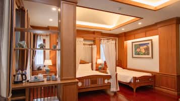 A hotel room with a wooden floor, a bed with a canopy, a bedside table with a lamp, a chair, a small table with a kettle, and a mirror with decorative items.