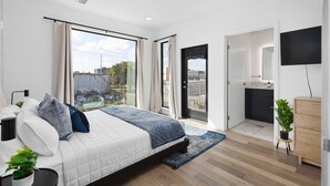 Ein modernes Schlafzimmer mit einem großen Bett, einem Fernseher und Blick auf die Stadt durch große Fenster.