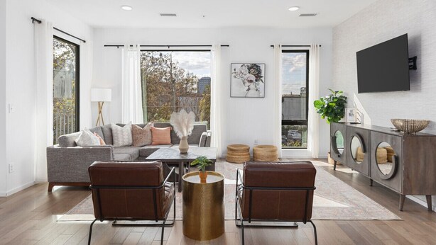 Ein modernes Wohnzimmer mit einem grauen Sofa, braunen Ledersesseln, einem Couchtisch und einem an der Wand befestigten Fernseher.